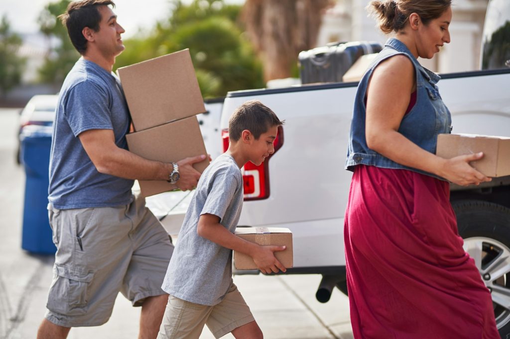 hispanic family moving boxes out of pickup truck into house